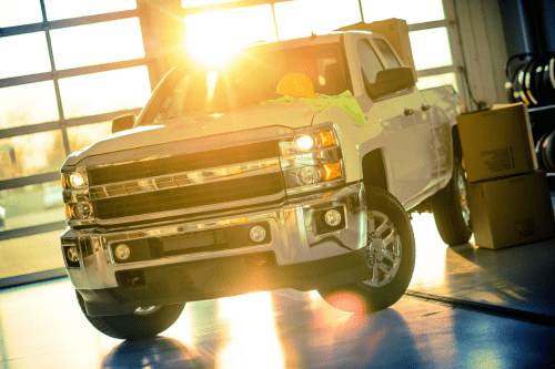 GM and GMC truck repair in Palmerston, Ontario, Canada with CDP Diesel. Image of white pickup truck parked sideways inside a shop with glass garage door with the sun shining through.