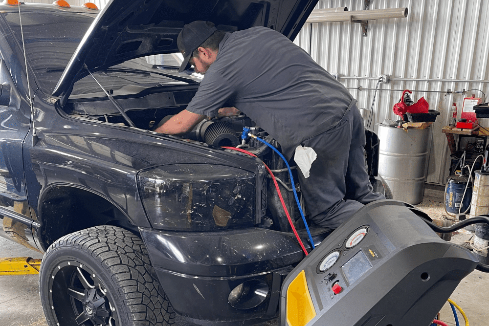 truck a/c & heater repair, diesel truck repair in Palmerston, ON at CDP Diesel & Auto. Image of a technician using A/C recovery and recharge equipment while servicing a black vehicle inside the repair bay.