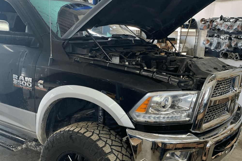 A lifted RAM 3500 diesel truck with off-road tires and aftermarket wheels is undergoing diesel engine maintenance at a CDP Diesel & Auto repair shop in Palmerston, ON, with its hood open for service.