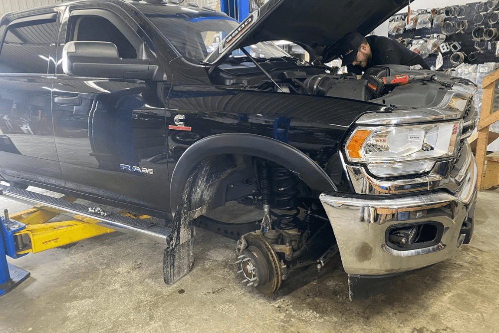 Truck maintenance in Palmerston, ON by CDP Diesel & Auto. Image of a black RAM Cummins on a lift with the front wheel removed while a mechanic performs engine diagnostics, highlighting expert diesel maintenance and repair services.