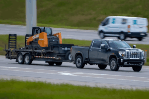 Trailer repair in Palmerston, ON by CDP Diesel & Auto. Image of a heavy-duty GMC pickup towing construction equipment on a highway, showcasing diesel performance, towing capability, and fleet service reliability.