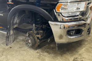 Brake replacement, diesel repair in Palmerston, ON by CDP Diesel & Auto. Image of a Ram truck on a lift with the front wheel removed, showing coil spring, shock, and brake components during heavy-duty diesel service.